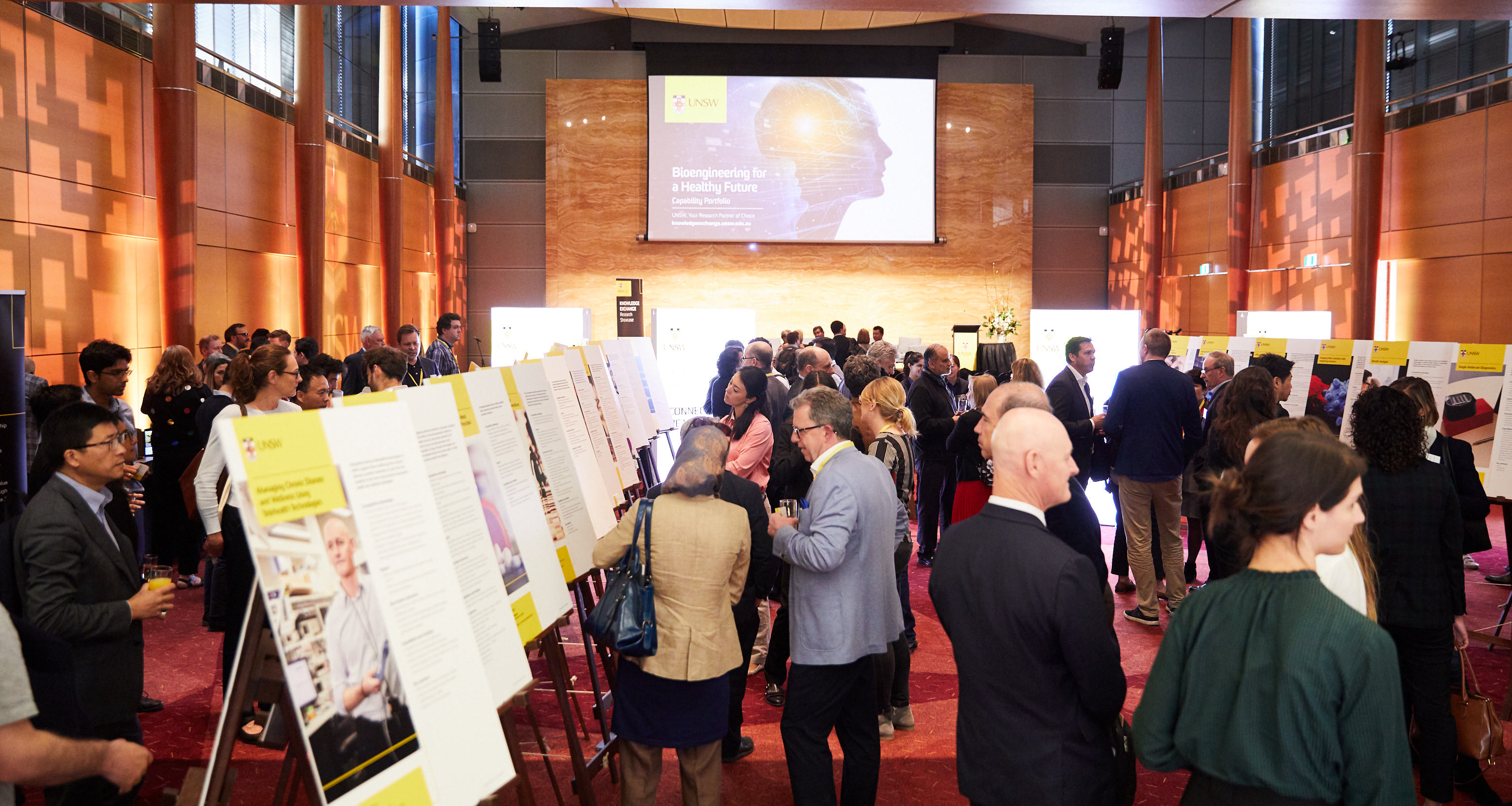 A crowd of people in a large room looking at information on cardboard posters