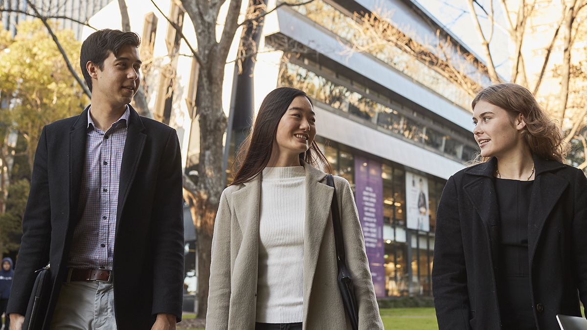 Three students wearing winter clothing walking on lower campus
