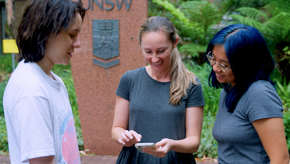 Three students looking down at a smartphone