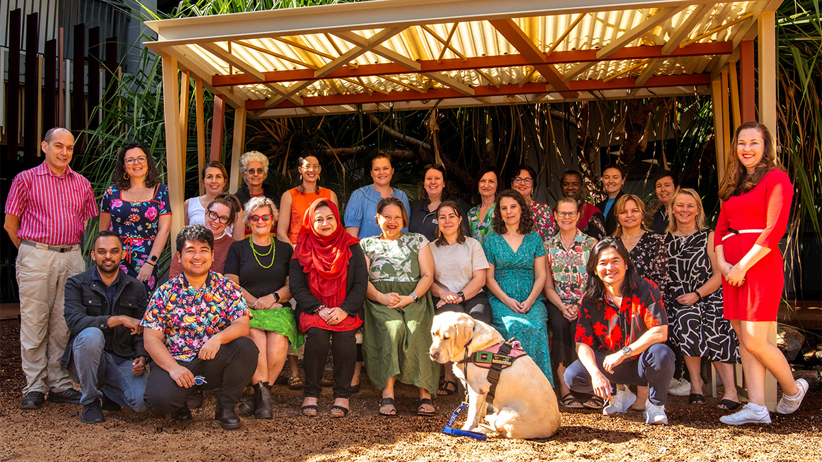 A large group of course attendees posed beneath a wooden shelter at Charles Darwin University 