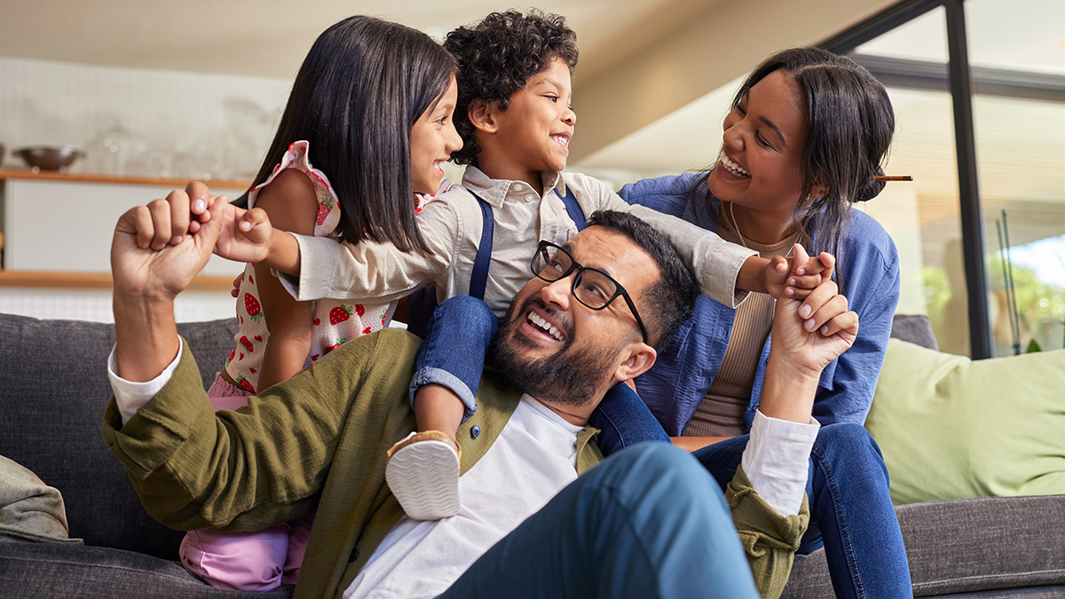 A family smiling together, with the kids and mum on a sofa and dad on the floor in front of them