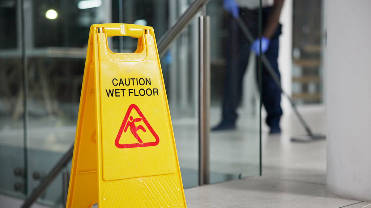 A yellow sign showing the words "Caution wet floor" with a blurry person mopping in the background