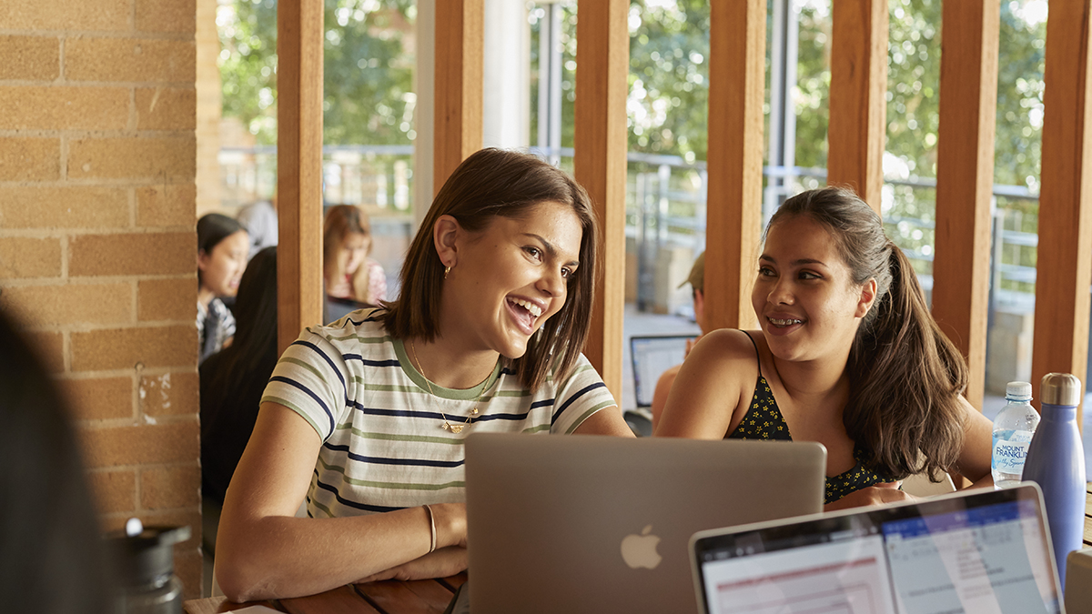 Two students smiling while using a laptop