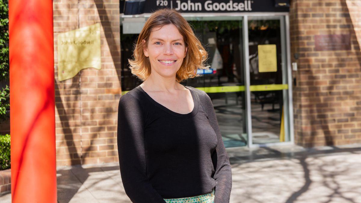 A woman wearing a black jumper stands out the front of a building