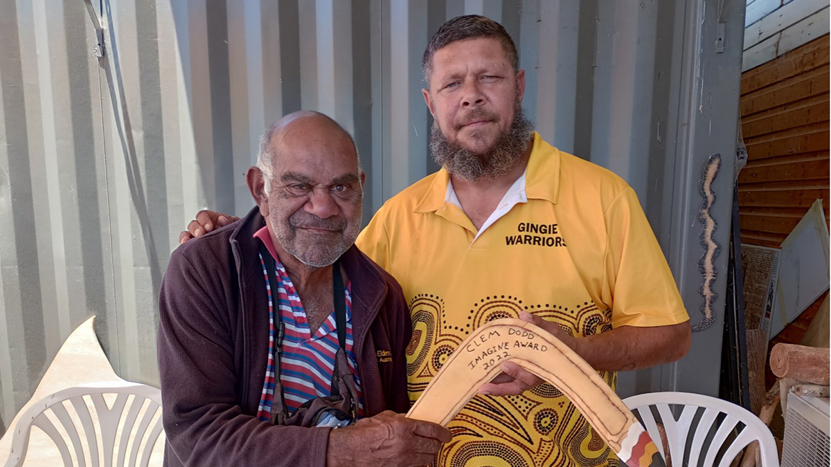 Clem Dodd (Dharriwaa Elders Group [DEG] Speaker) is presented with a bubarraa (fighting boomerang) by Steven “Bungee” Dennis, a Dealing with Fines team member at the DEG.