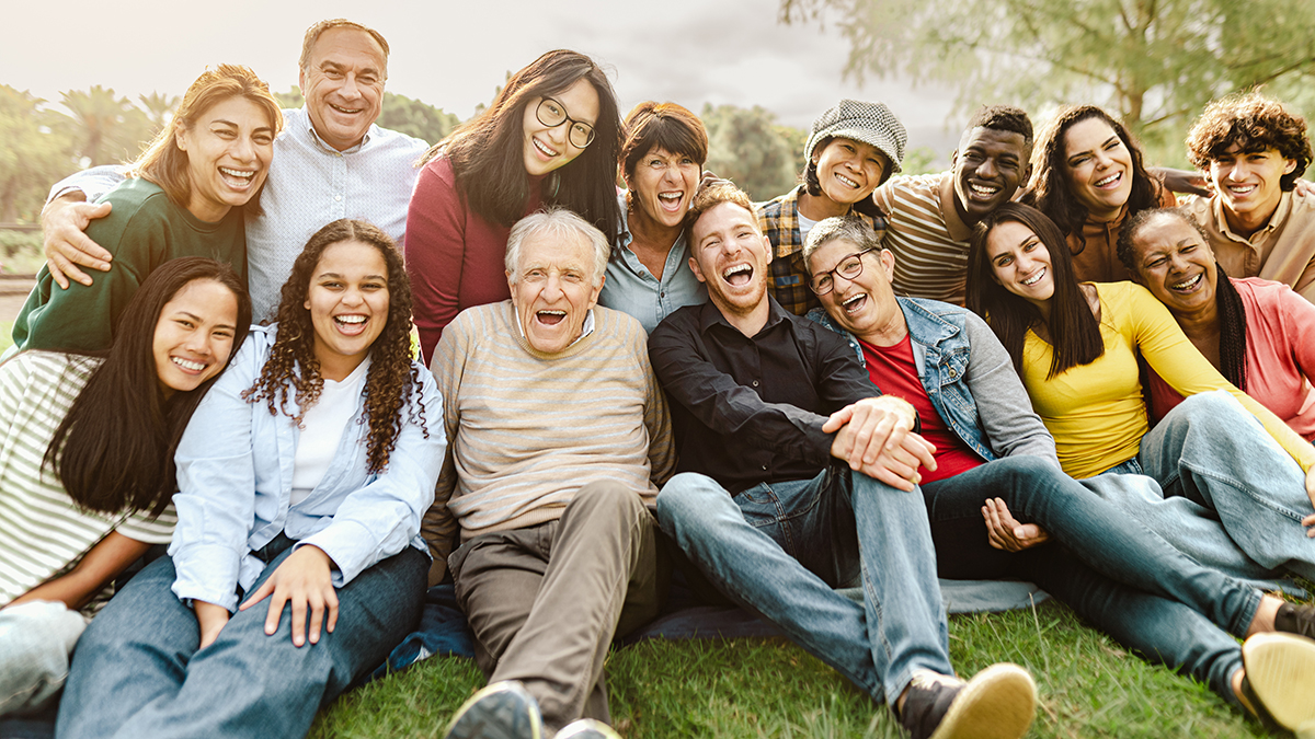 A group of smiling people sitting on grass with an elderly man at the centre