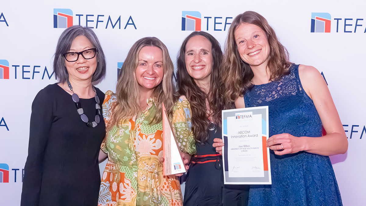 Four women smiling while one holds a certificate
