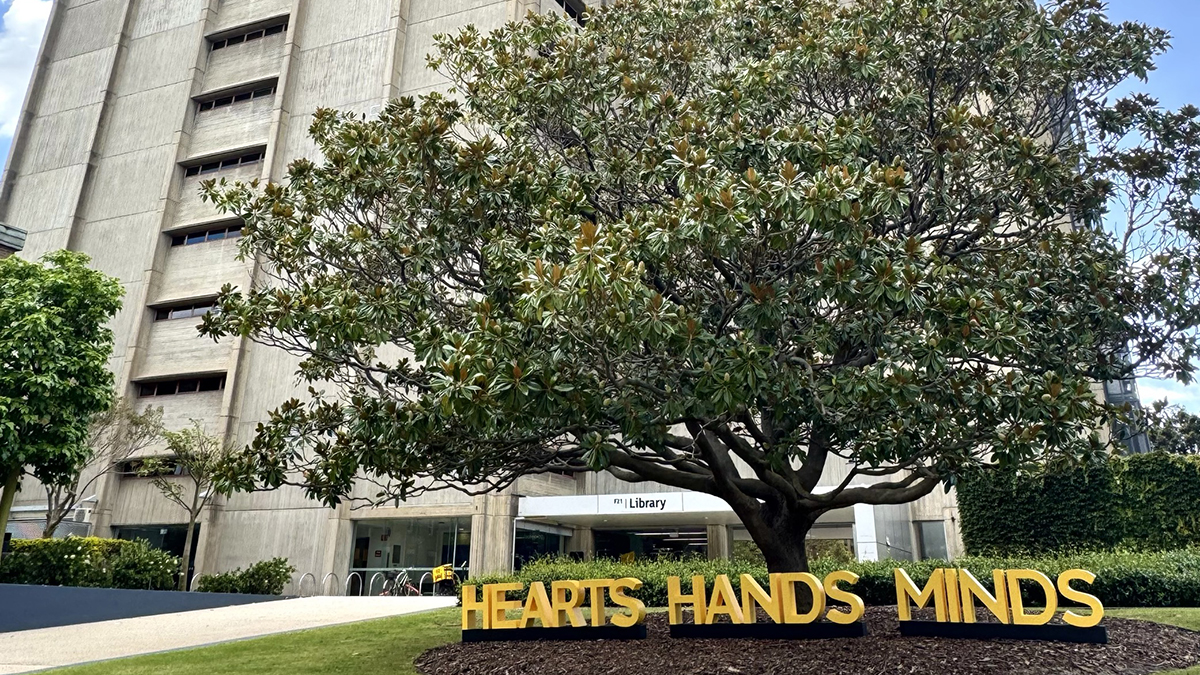Tree with large letters in front spelling "Hearts Hands Minds"