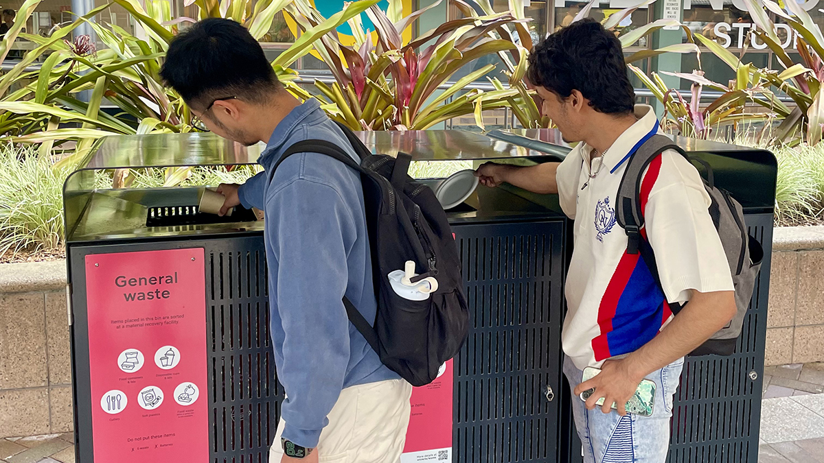 Two students putting rubbish in a bin