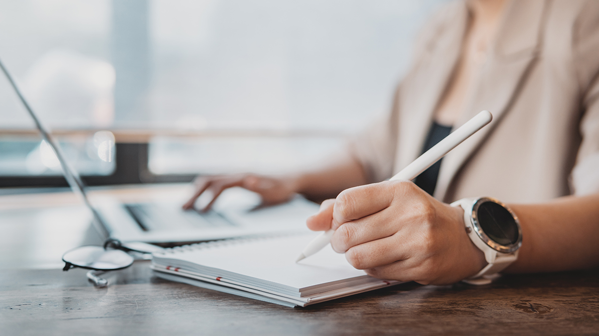 Close up of woman writing in notebook beside laptop