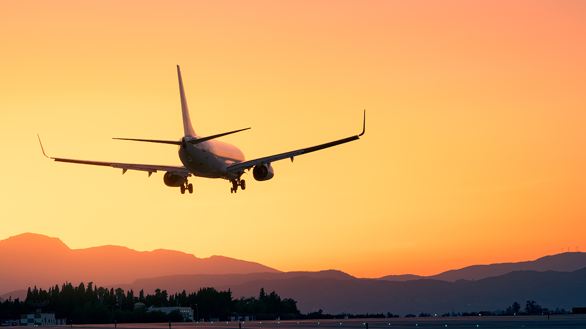 An airplane in silhouette against an orange sky