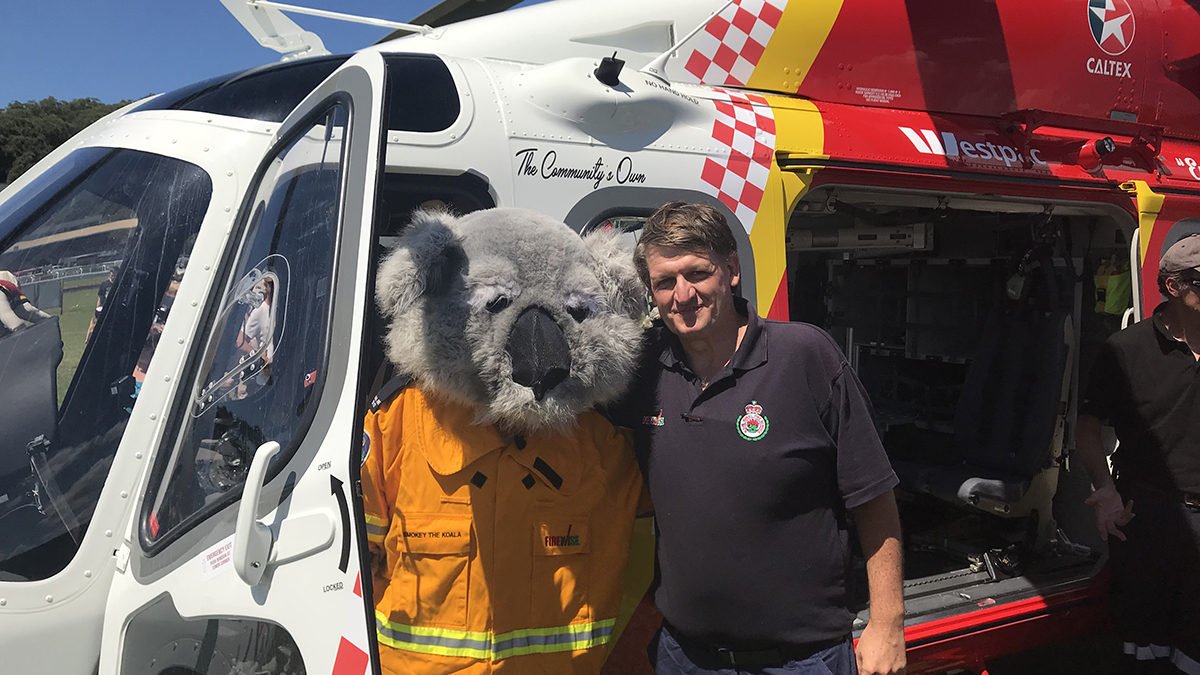 Mark Griffith standing beside a person in a koala suit in front of a rescue helicopter