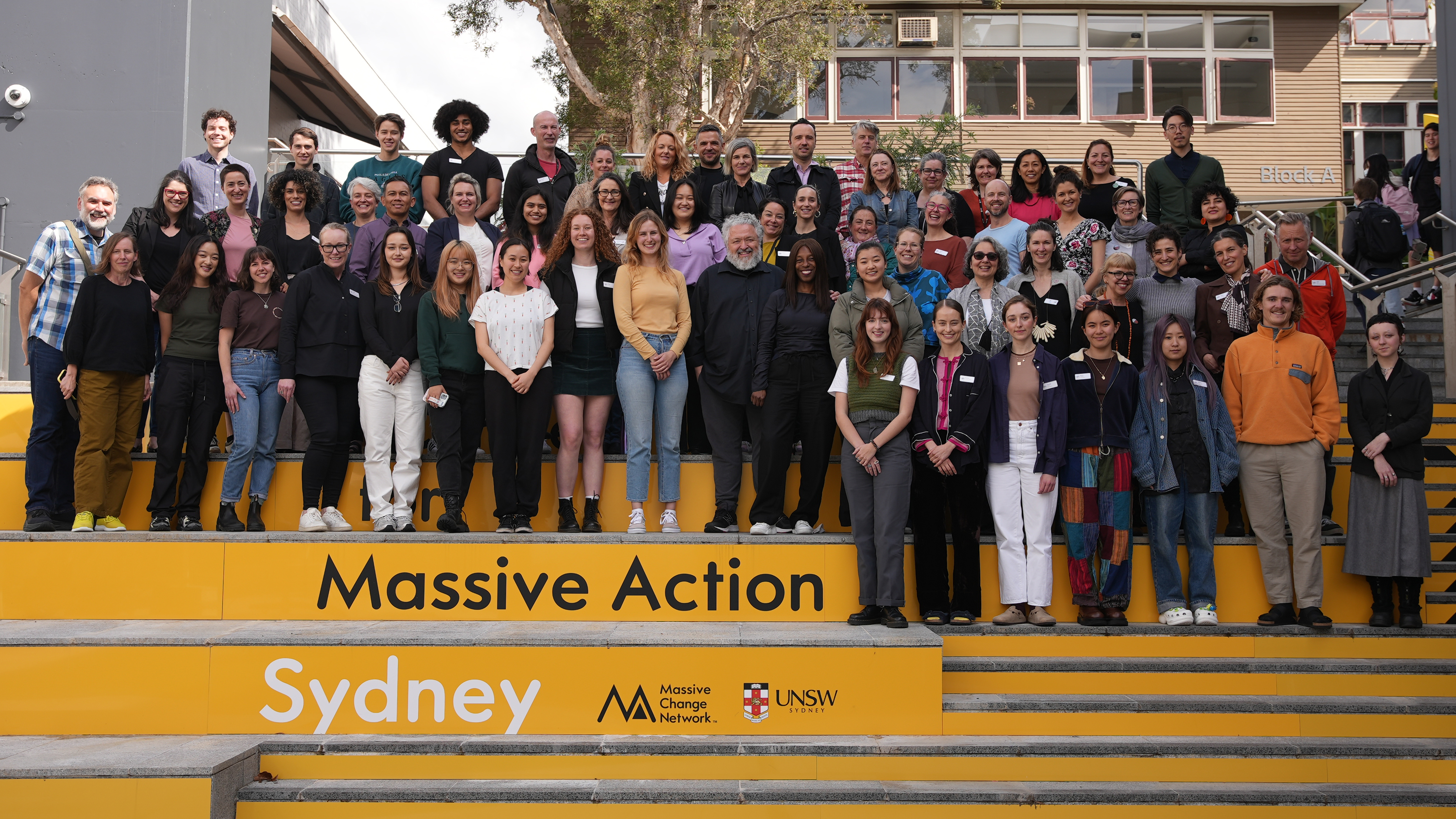 Large group of people standing on yellow steps reading Massive Action Sydney