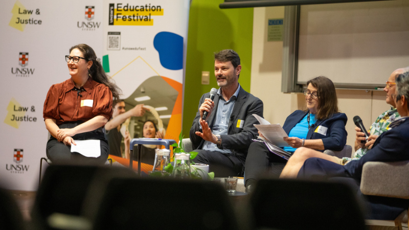 A man holds a microphone sitting beside two women wearing glasses for a panel discussion