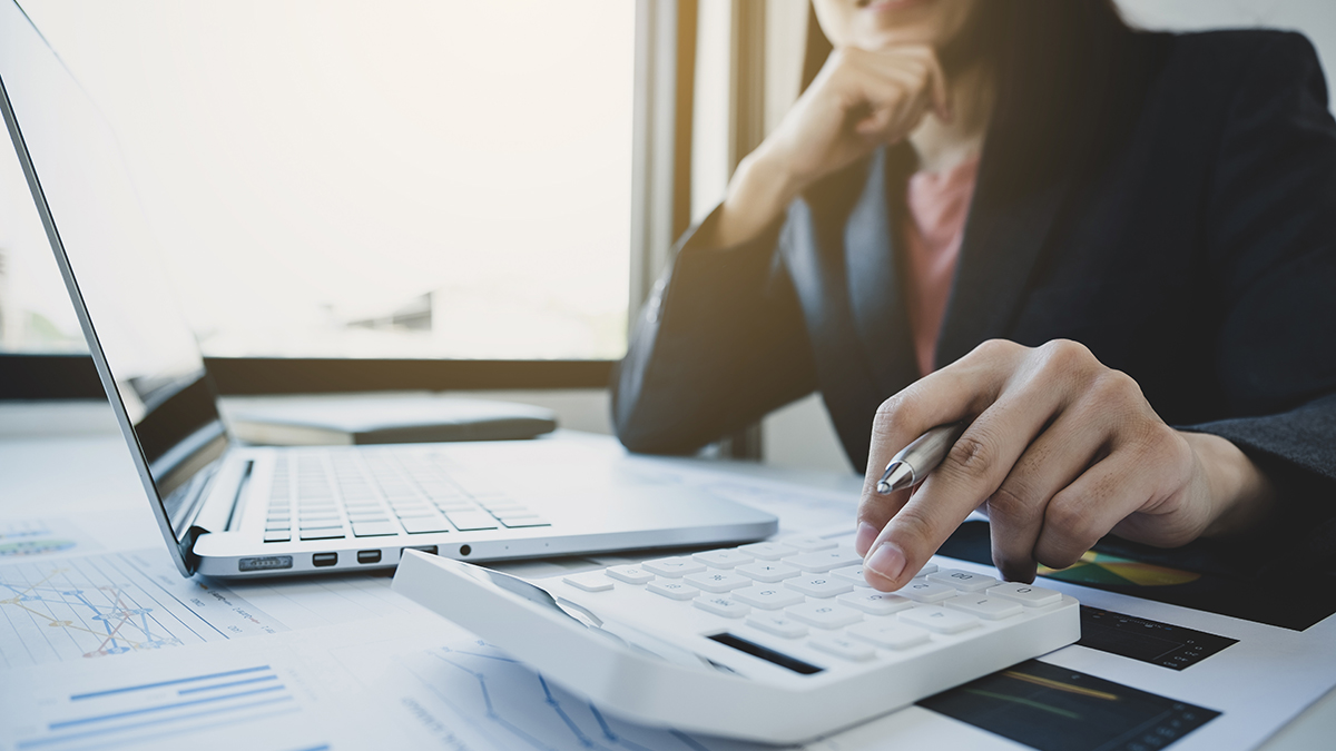 Laptop and calculator on a desk with woman's hand on calculator