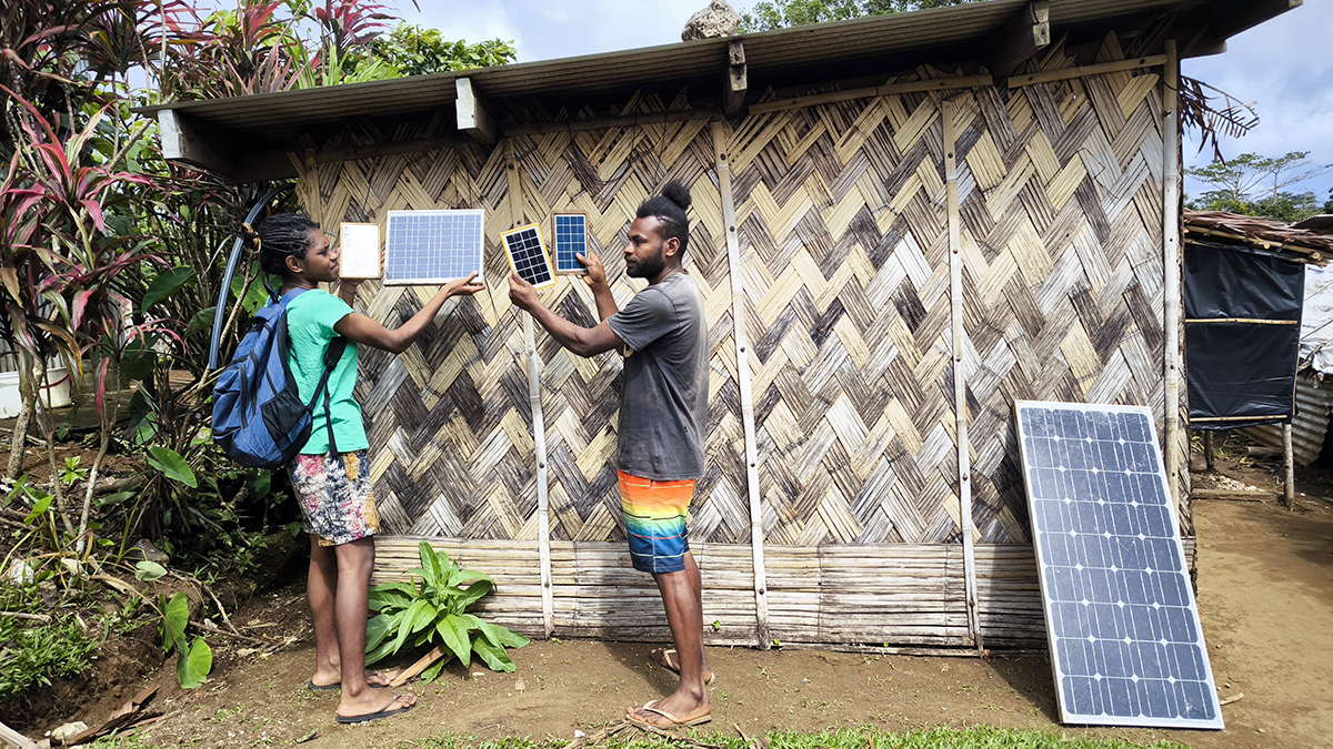 Two people standing and holding small solar panels outside a building