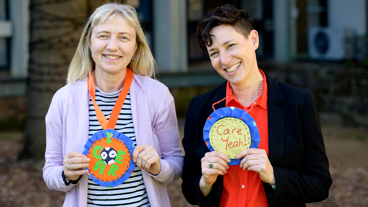 Two women smiling and wearing paper rosettes