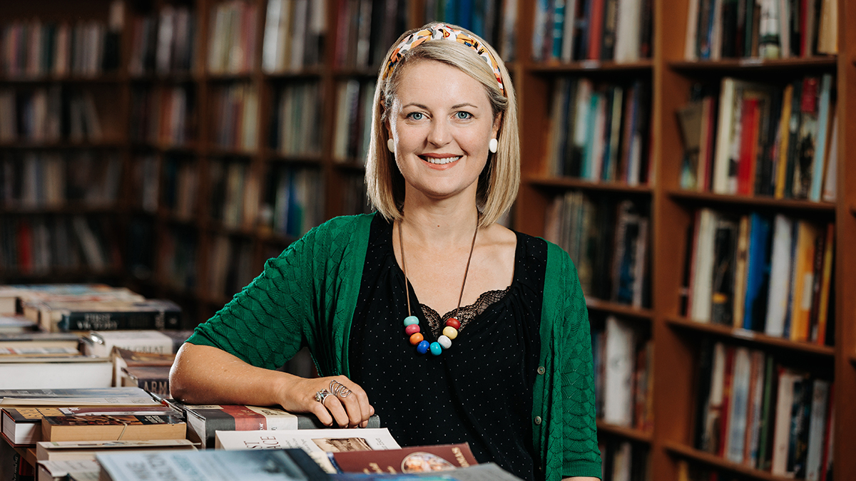 Sarah Sassoon in front of a bookshelf at a table covered in books