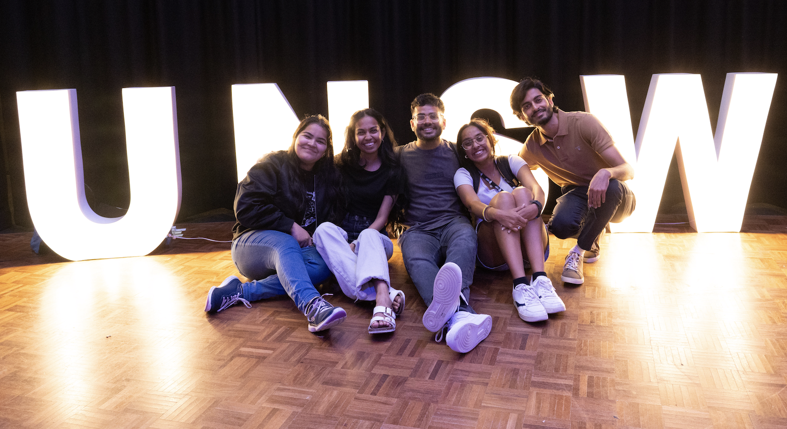 students sitting in front of an illuminated UNSW sign