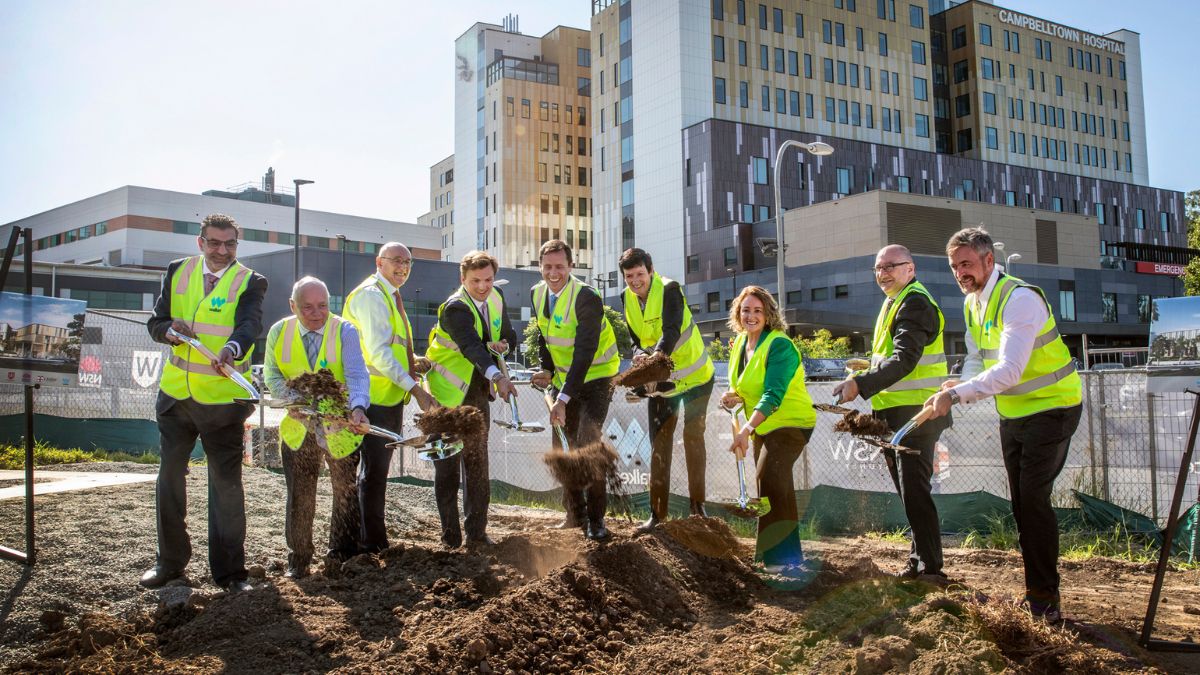 A group of men and women in hi-vis vests shovel dirt on an urban construction site.