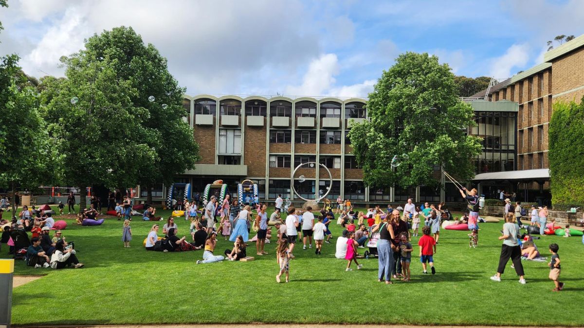 Crowds of adults and children gather for games on a lawn in front of a three-story building