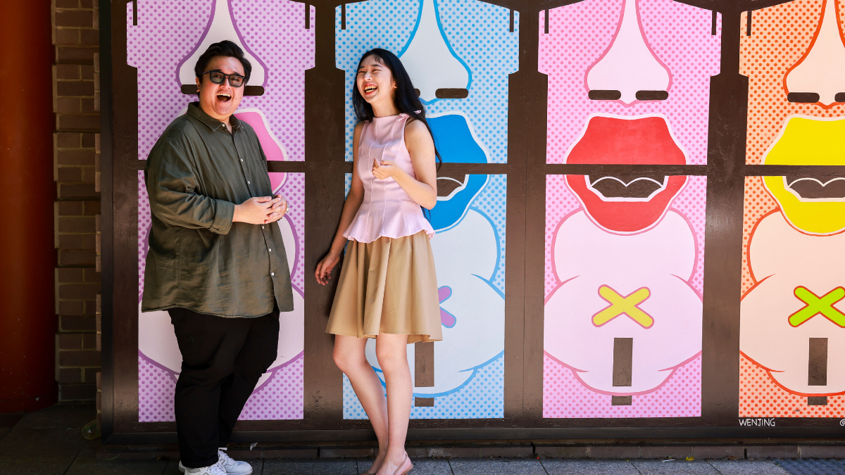 Two people standing and laughing in front of a pop art painted wall.