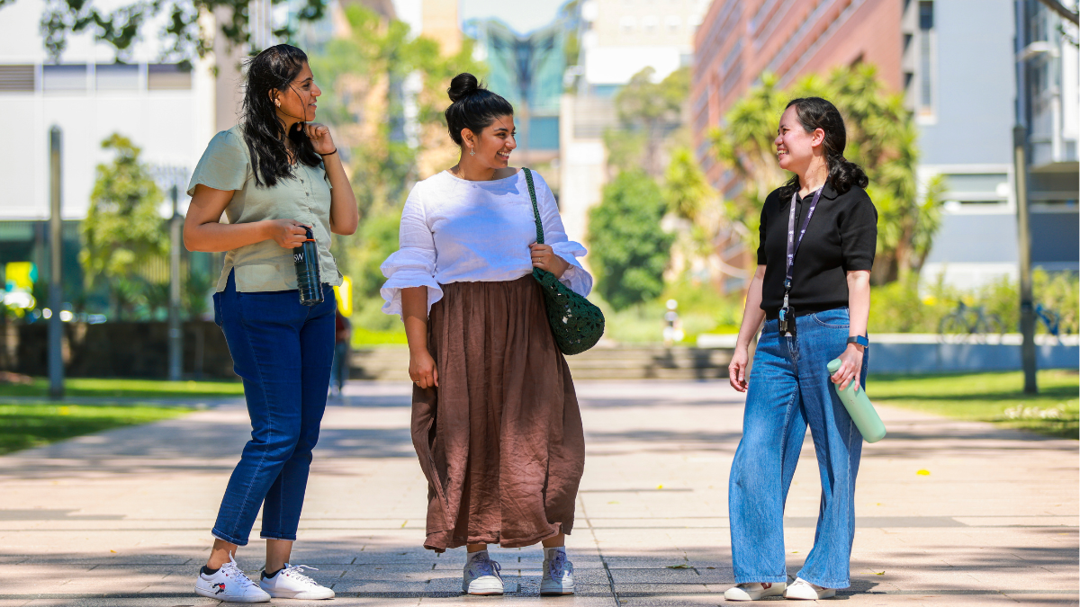 Three women standing on campus talking and smiling.