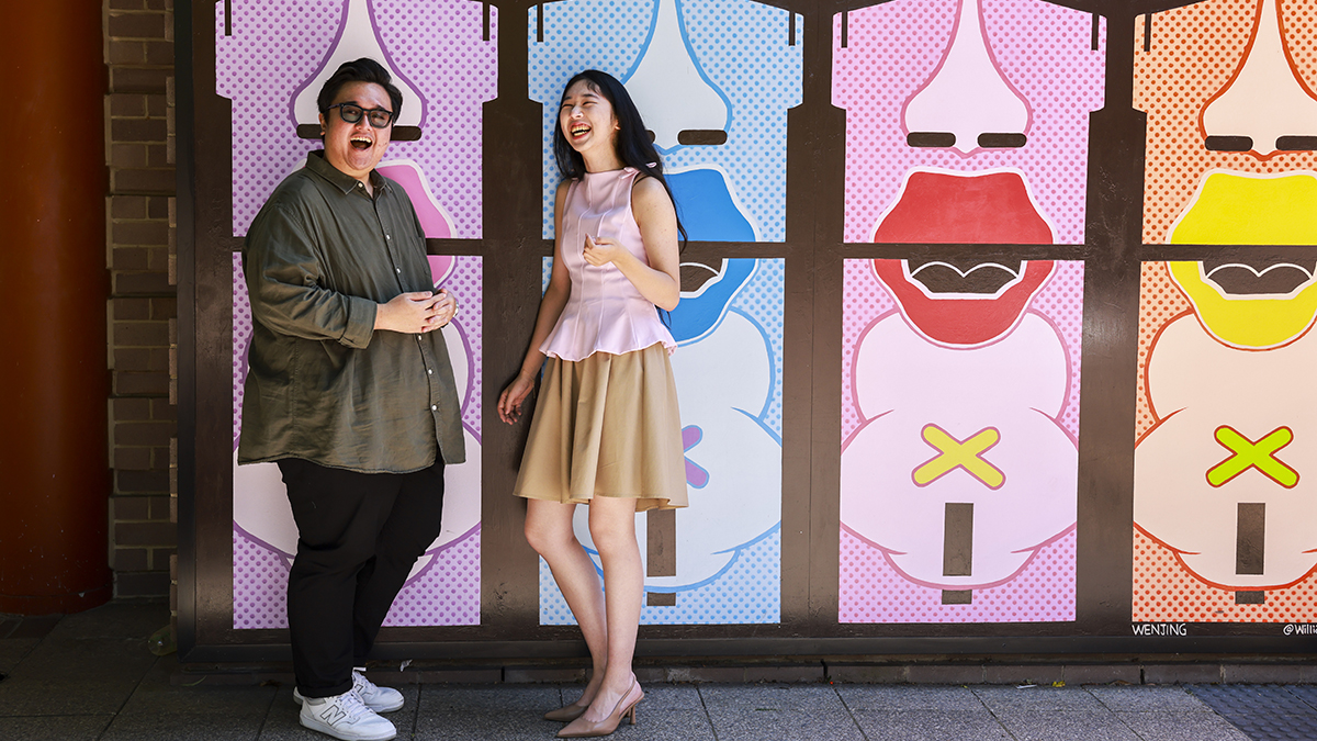 Two people standing against a colourful wall