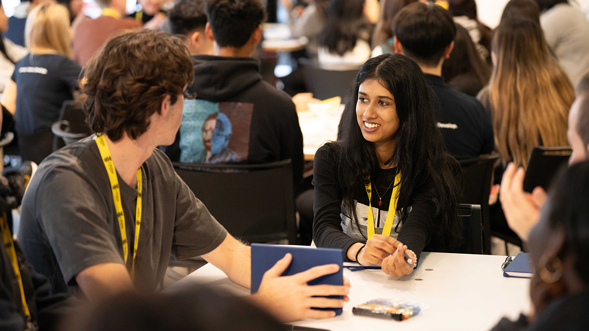 A group of people wearing yellow lanyards sit at tables