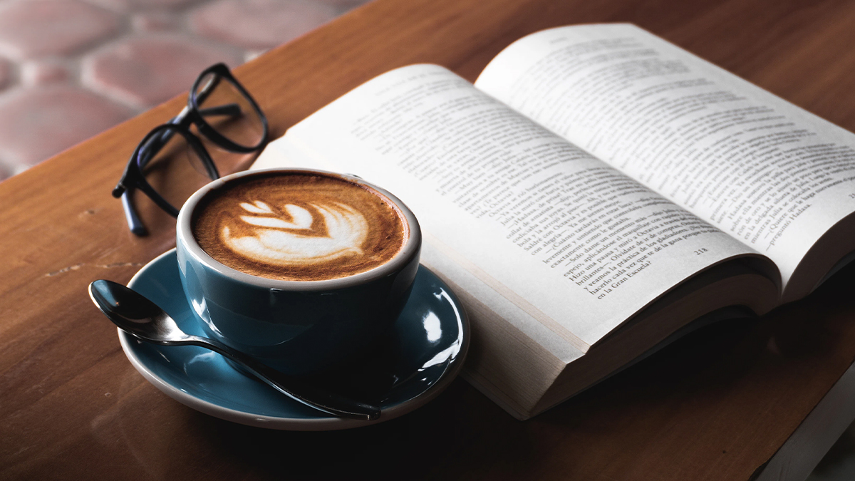 A cup of coffee, open book and glasses on a table