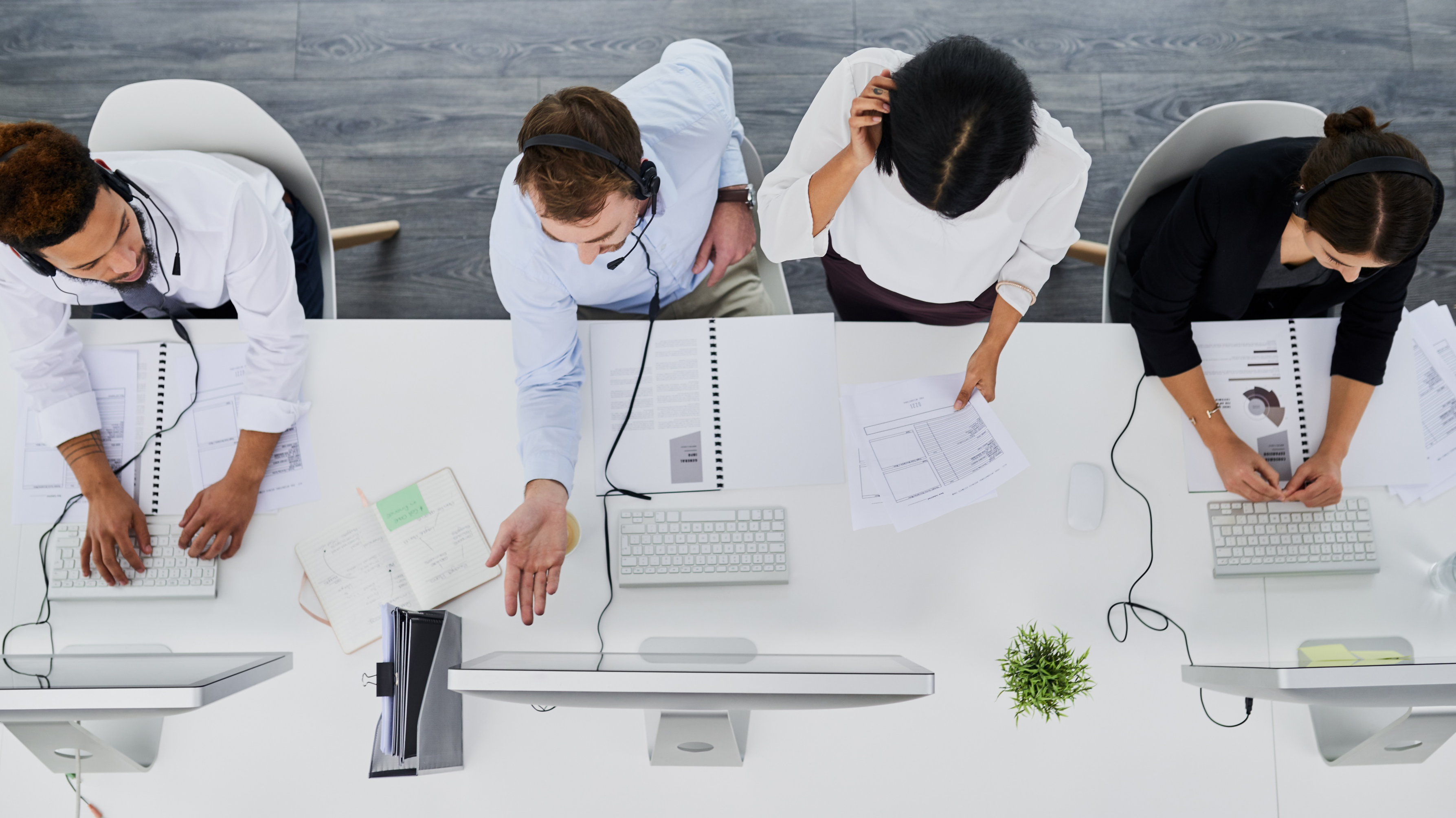 View from above of four people sitting at a white desk working on computers