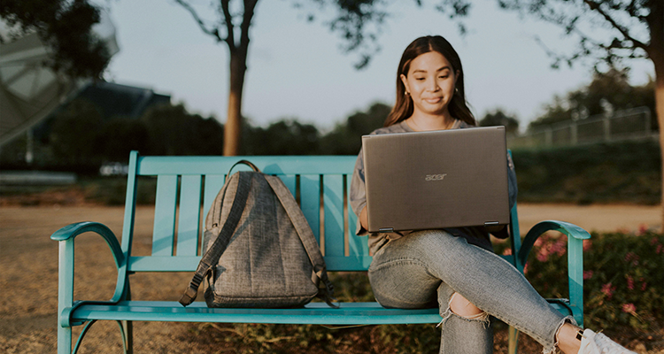 Student using a laptop on park bench