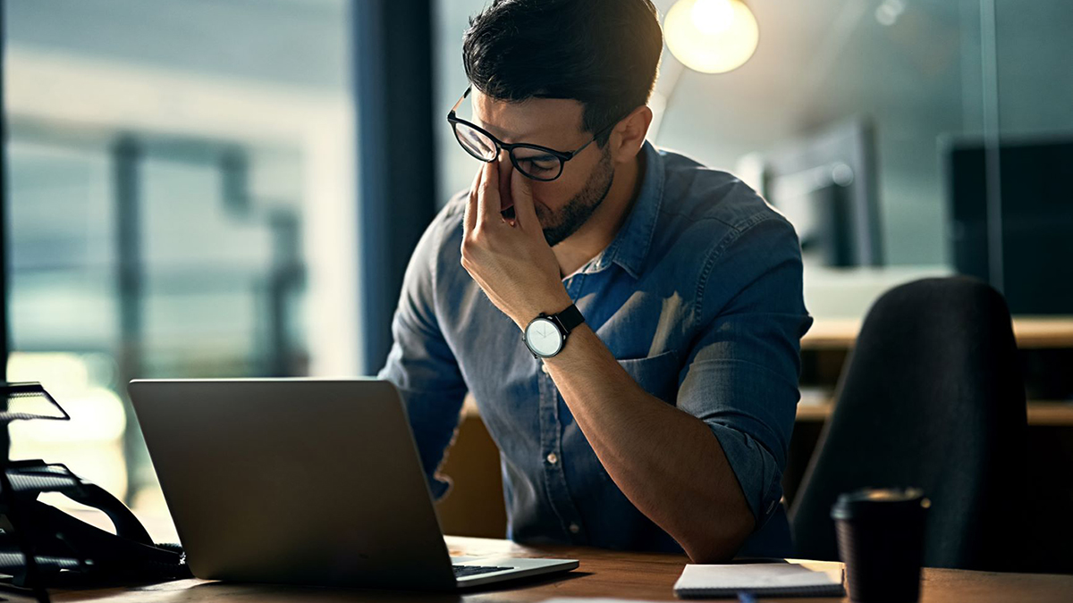 A man sits at a desk with his hand at his face looking stressed