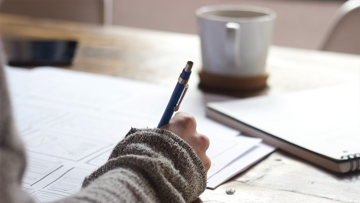 Person writing with a cup of coffee on their desk