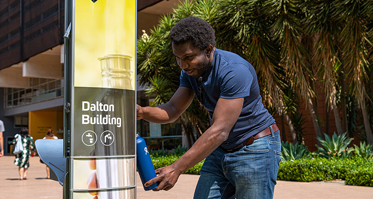 Man filling up drink bottle from UNSW bubbler on University Mall