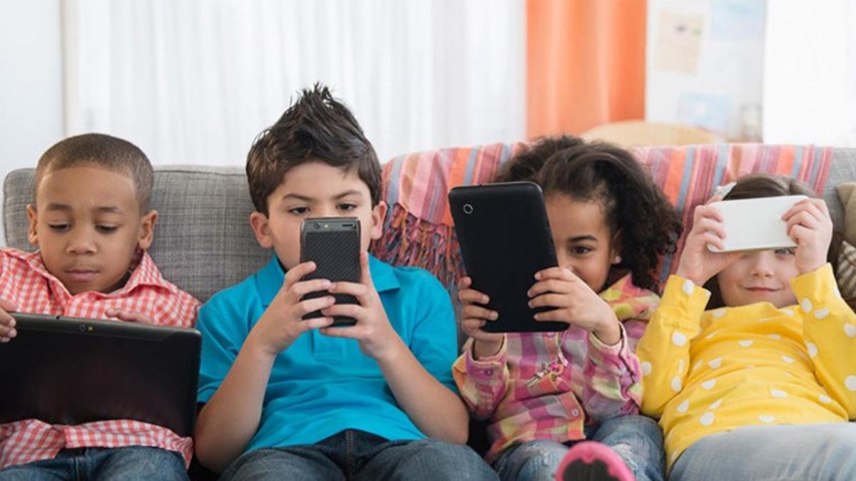 Four children on a sofa using devices