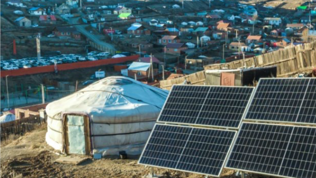 A solar panel next to a hut on the outskirts of a town.