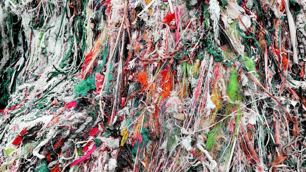 A close-up of a large tangled mass of multicolored threads, fabric scraps and textile waste