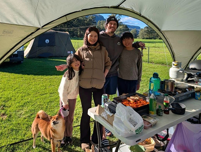 A young girl, woman man and boy standing in the entry to a tent in a field