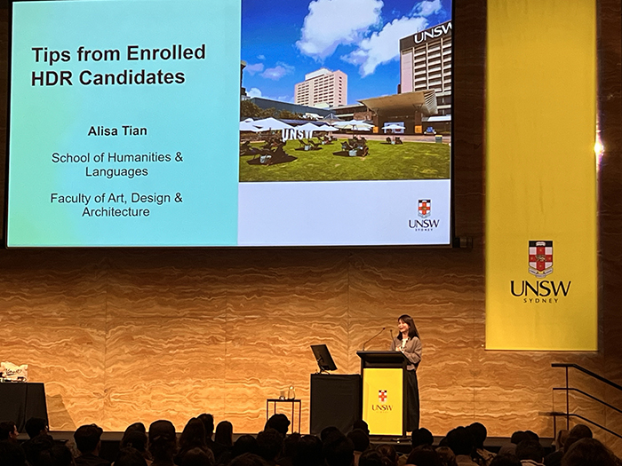 Alisa Tian on stage in front of a slide that says "Tips from Enrolled HDR Candidates"