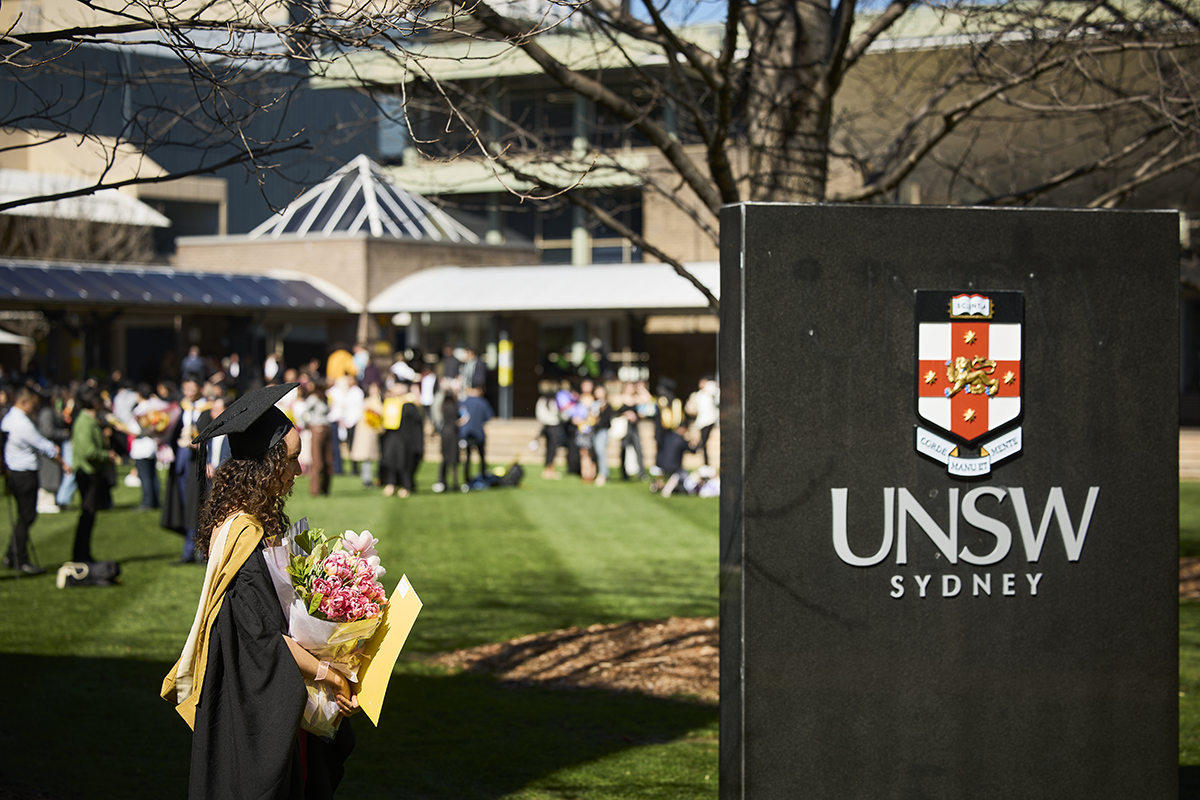A student walking across the library lawn with a UNSW sign to the side