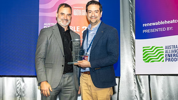 Two men standing holding an award against banners for renewable energy