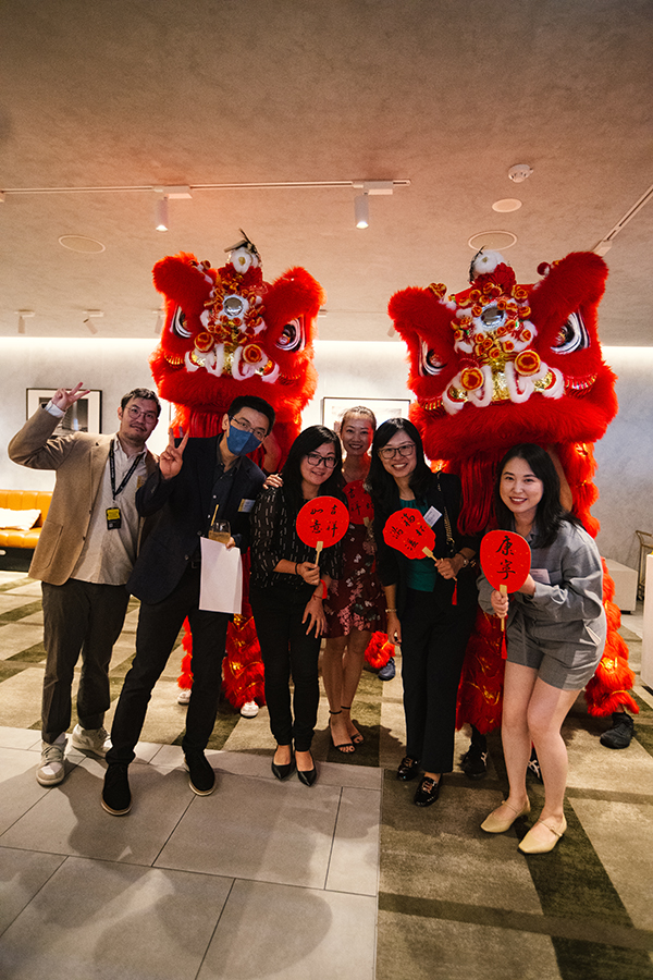 A group of people holding red fans in front of two red Chinese lion dancers