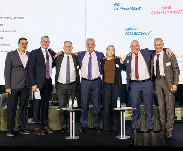 Seven people with arms around of each other in front of a screen showing illustrated statements