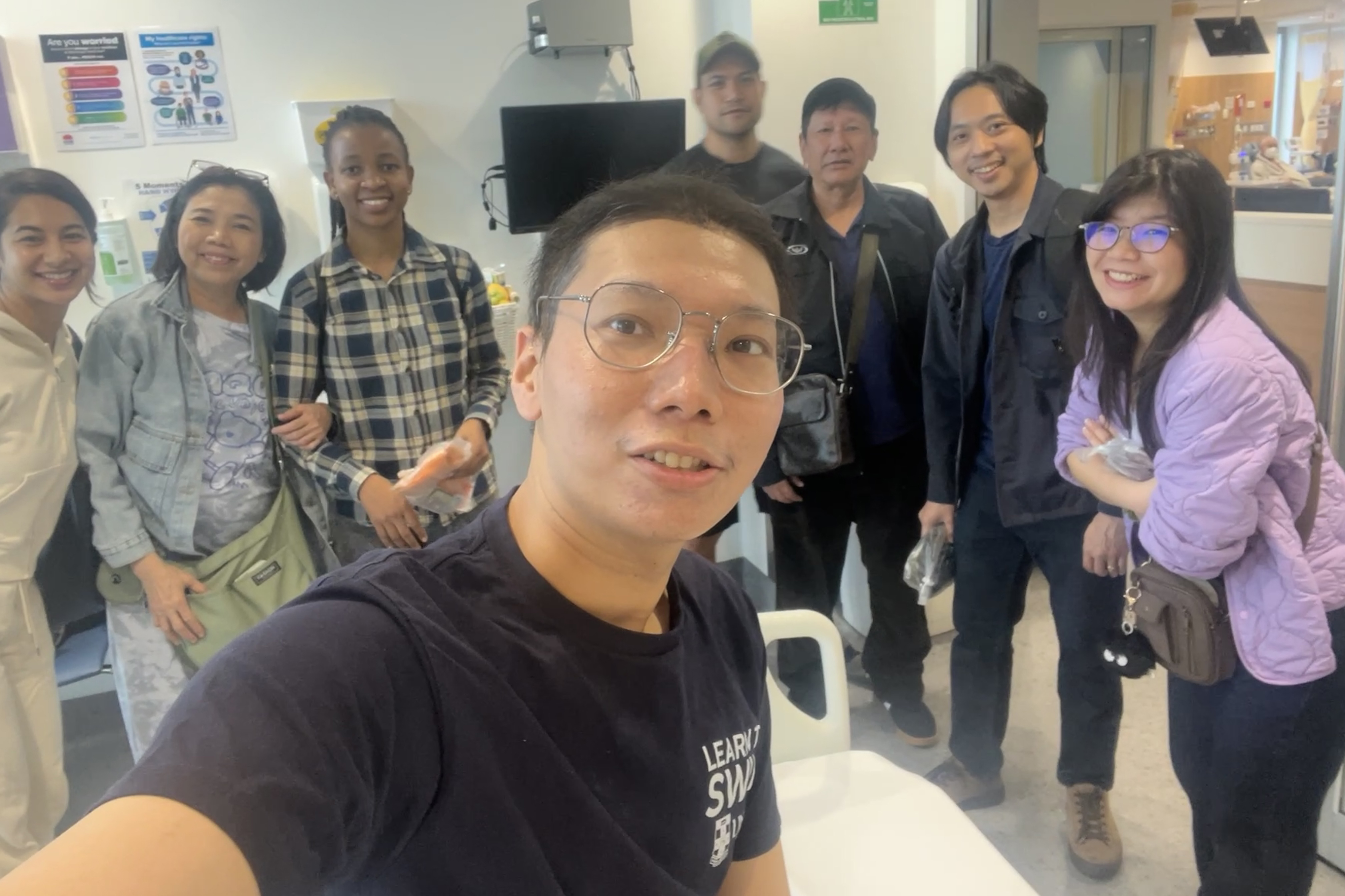 A young man in glasses taking a selfie with a group of friends behind him