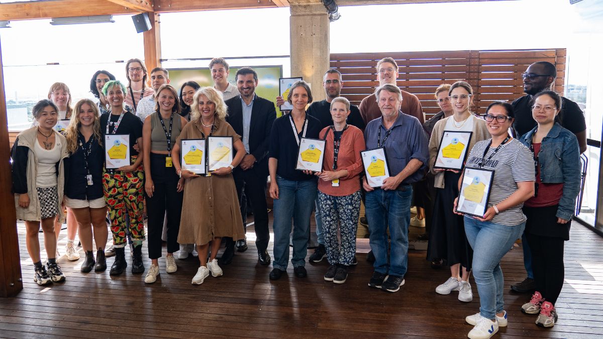 A diverse group of people stand on an outdoor deck and hold framed certificates.