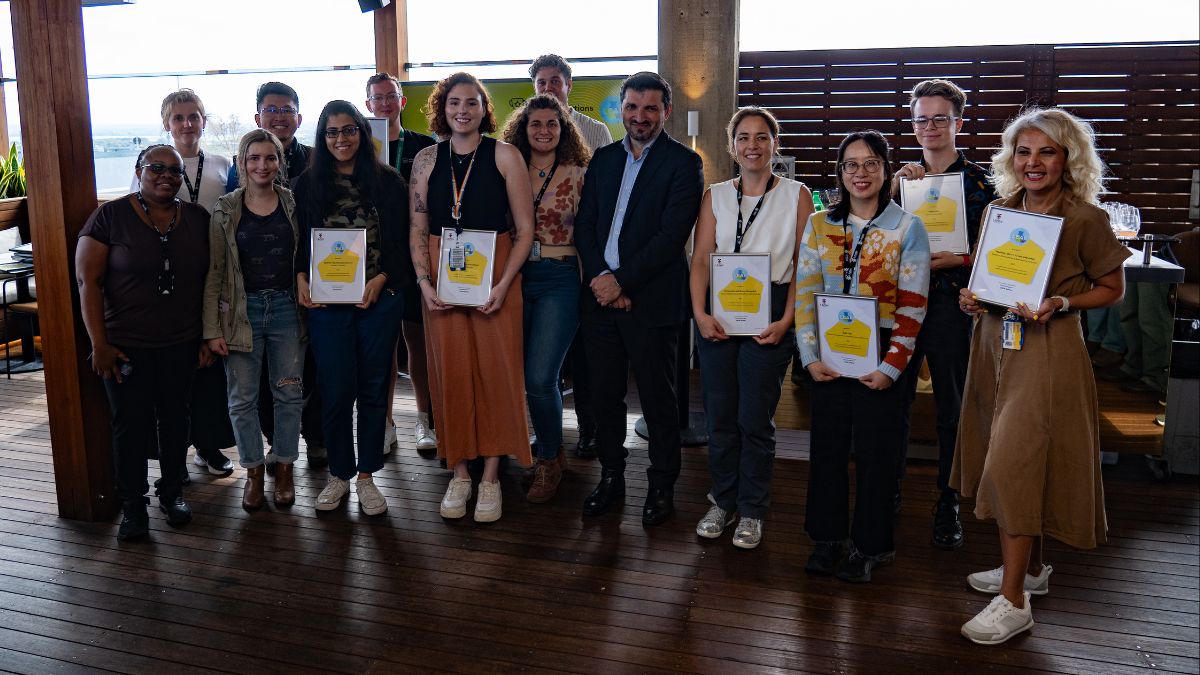 A group of men and women stand together on a wooden deck holding framed certificates