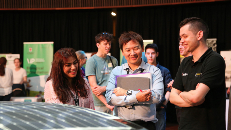 A woman and two men look at a display in an exhibition hall.