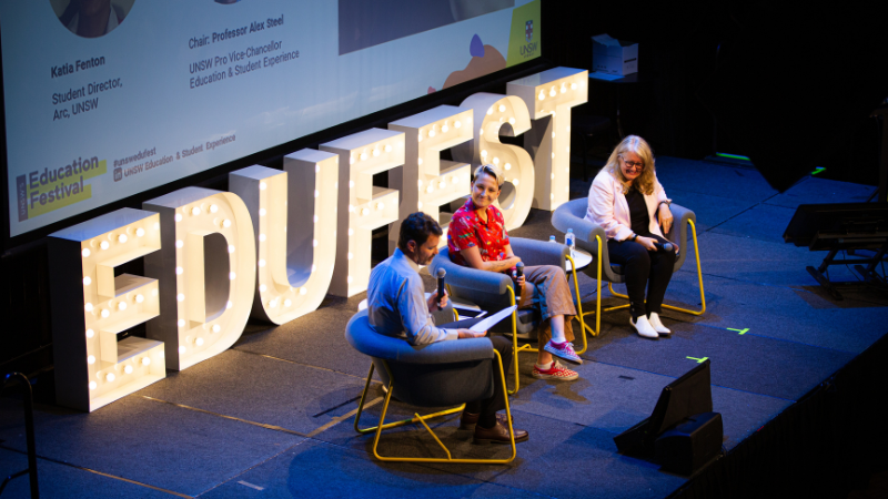 A man with a microphone and two women sit on stage in front of the letters EDUFEST for a panel discussion