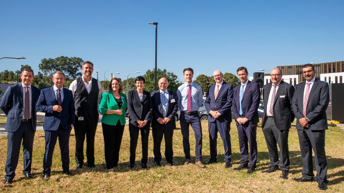 A group of men and women in suits stand in a line on the grass